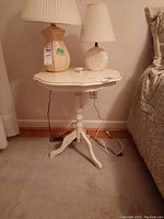 View of the wood side table with two lamps placed on top; shows the scalloped edge tabletop and painted cream color.