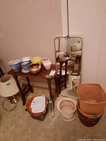 Entire lot including side table, ceramic pots, baskets, table lamp, wood slice trays, glass vase, and framed wall mirror reflected behind.