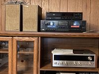 Overview of shelving unit displaying audio components: pair of speakers on top left, Sony CD player on top right, JVC cassette deck on middle shelf, Pioneer receiver below