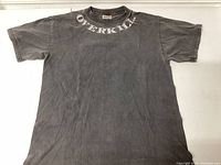 Front of vintage black Overkill T-shirt, showing faded black cotton fabric with white OVERKILL text around the collar.