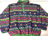 Front view of a vibrant XXL fleece pullover with geometric pattern in green, purple, pink, and yellow, showing elastic cuffs and hem, and half-button green placket at collar.