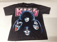 Front view of black KISS T-shirt with large graphic of the four band members' faces and the pink KISS logo on the chest.