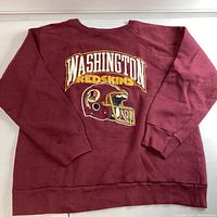 Front view of maroon vintage Washington Redskins sweatshirt with large printed graphic and text.
