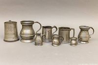 Full view of seven pewter vessels in a row showing size and variety