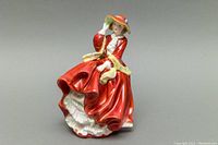 Front view of the Royal Doulton porcelain figurine featuring a woman in a red dress and orange hat holding her hat.