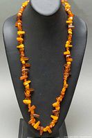 Full view of 30-inch amber nugget necklace on display bust showing bead variety and length.