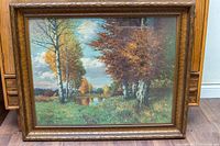 Framed print showing full artwork with trees, river, and sky in carved wooden frame with minor wear.