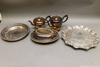 Wide view showing all silver plated servingware items including two teapots and three trays with visible tarnish and wear.