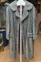 Full length front view of the vintage Persian lamb fur coat hanging on a mannequin with surrounding background showing room details.