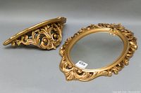 Two ornate vintage gold painted wall pieces: an oval mirror and a matching wall sconce with detailed carvings.