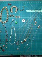 Full view of assorted costume jewelry on a green cutting mat with measurement grid showing variety and layout.