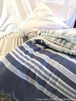 Photo showing folded striped comforter and white European pillow on bed.