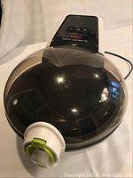 Top angle showing closed air fryer with digital control interface on top and round black cooking chamber with clear plastic lid.
