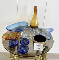 Full view of all glass decor items arranged on a round glass table showing color, shape, and sheen.