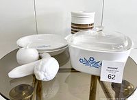 Photo showing assortment of Corning Blue Cornflower pie plates, covered casserole with lid, coffee jar, and white ceramic fruit decor.