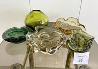 Photo showing all six pieces including assorted green and amber ashtrays and one green glass vase on a glass top table.