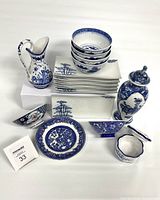 Overall front view of the mix of Blue Willow and Chinoiserie style blue and white porcelain pieces including plates, bowls, pitchers, vases, and small containers.
