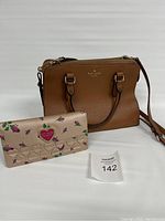 Full view of the Kate Spade leather handbag and Betsy Johnson wallet together on white background with lot number card