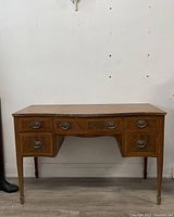 Front view of vintage wooden desk vanity with five drawers, original metal oval drawer pulls, and tapered legs.