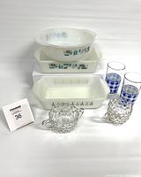 Full lot view showing all items grouped together: two patterned Fire King bowls, one rectangular baking dish with botanical pattern, two blue check pattern drinking glasses, and a clear glass honeycomb textured milk and creamer set.