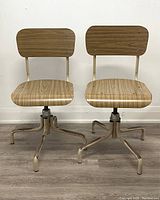 Front view of two identical industrial swivel stools showing wood grain laminate seats and backs, metal bases with 4 legs each.