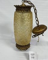 Full view of amber textured glass swag hanging light with metal top, bottom, and hanging chain.