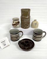 Front and slightly above view of entire pottery set including 2 striped mugs, 3 different sized vases and a dark brown candle holder, with a white background.