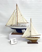 Two vintage model sailboats, one blue and white and the other natural wood, both with canvas sails mounted on wooden bases.