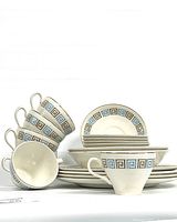 Stack of cups, saucers, bowls, and plates showing Greek key pattern in blue, brown, and gold