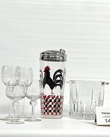 Front view of four crystal glasses, glass ice bucket, and tall glass and metal rooster printed drink shaker.