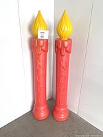 Front view of two tall vintage red blow mold candlesticks with yellow flame tops and NOEL embossing.