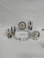 Front view of vintage MCM catch-all dish, three glasses with building motifs, glass inkwell, and round alarm clock