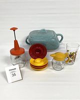 Overview of all vintage kitchen items including ceramic dish, hand chopper, egg cups, syrup container, and tall glass with bird print.