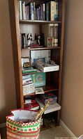 Full view of the wooden bookshelf showing books, decorative bells, cards, boxes, and gift items arranged on multiple shelves and a patterned gift bag on the floor.