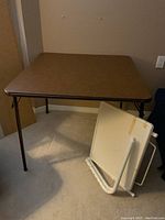 Brown square folding card table set up on floor, foldable metal legs visible