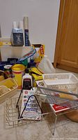 Photo showing metal baskets, cleaning products including Comet, Clorox wipes, glass cook-top cleaner, Finish Quantum, and a book about cleaning.