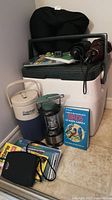 Photo showing all items in the lot including cooler, beverage jug, lantern, umbrellas, neck pillow, books, maps, and converter plug.