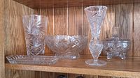 Overview of all crystal pieces on wood shelf showing two vases, bowl, candy dish with lid, and relish tray