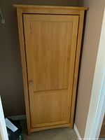 Front view of single door wooden cupboard in natural light wood finish with metal knob handle and paneled door design.