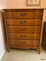Front view showing five drawers with metal handles, scalloped bottom edge, and curved Queen Anne legs.