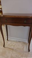 Front view of hall table showing scalloped top edge, drawer and curved legs