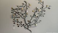 Full view of the metal wire wall art mounted on the wall showing overall shape and color of glazed medallion leaves.