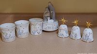 Full view of three ceramic candle holders with nativity scenes, the music box, and three ceramic bells with gold star toppers.