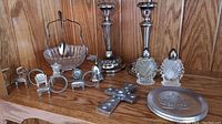 Wide shot showing all items including candle holders, salt and pepper shakers, napkin holders, decorative cross, and glass bowl with tongs arranged on a wood shelf.