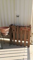 Wood pocket fence planter with plastic inserts alongside metal wire planter stand with plastic pot, outdoors near light-colored siding.