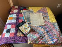 Overview of two quilts laid out with book, mini quilt square and magazines