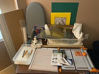 Tabletop overview showing Rowenta iron, ironing board, rulers in tub, cutting mat, paper cutters, tracing paper and tools