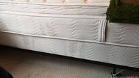 Side view of the twin mattress and boxspring on the metal bed frame showing the white quilted fabric and caster wheels on the frame.