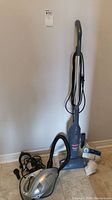 Full view of Bissell Magic Back upright vacuum and Dirt Devil Scorpion handheld vacuum on floor with power cords and spare filters.