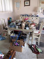 Dining table with numerous small items placed on top, showing table and chairs with light distressed finish.